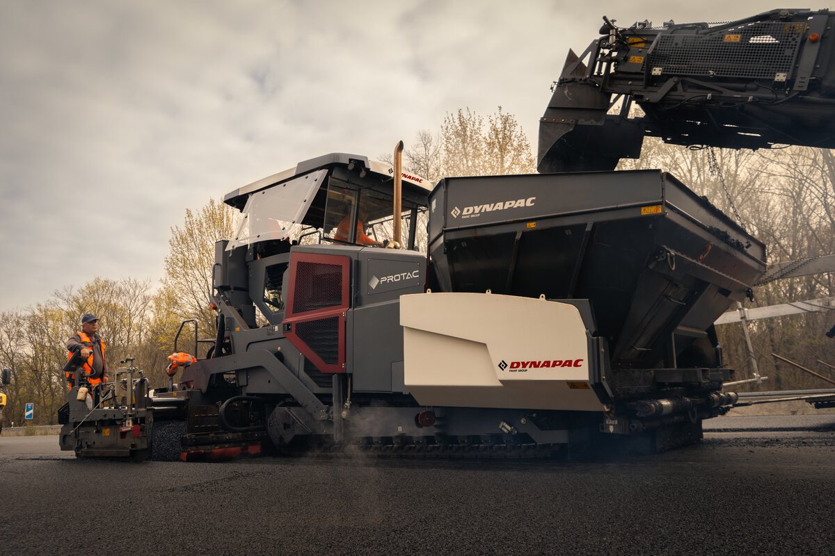 Close-up of a Dynapac asphalt paver being optimized by a mobile feeder, ensuring a seamless paving process and eliminating temperature segregation